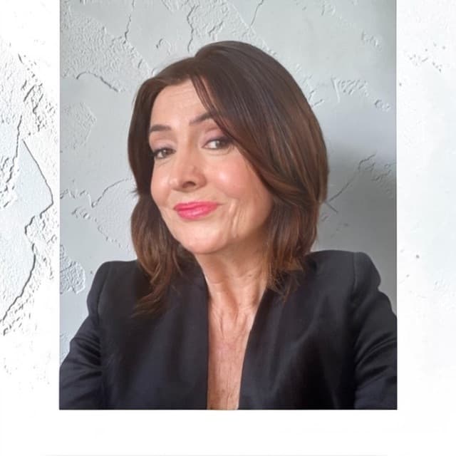 Woman with shoulder-length brown hair and pink lipstick wearing a black blazer against textured wall.